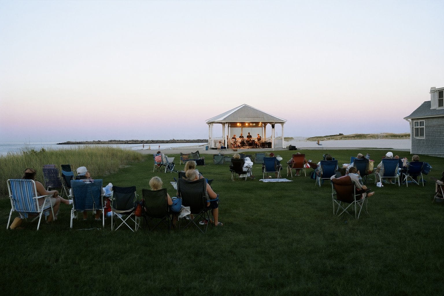 Illustration: lawn chairs on the grass facing a small pavilion stage at dusk