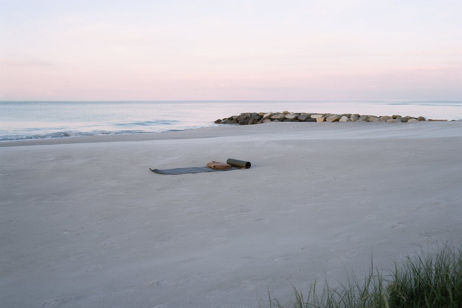 Illustration: a yoga mat and towel on an empty beach at sunrise with a rock jetty in the distance